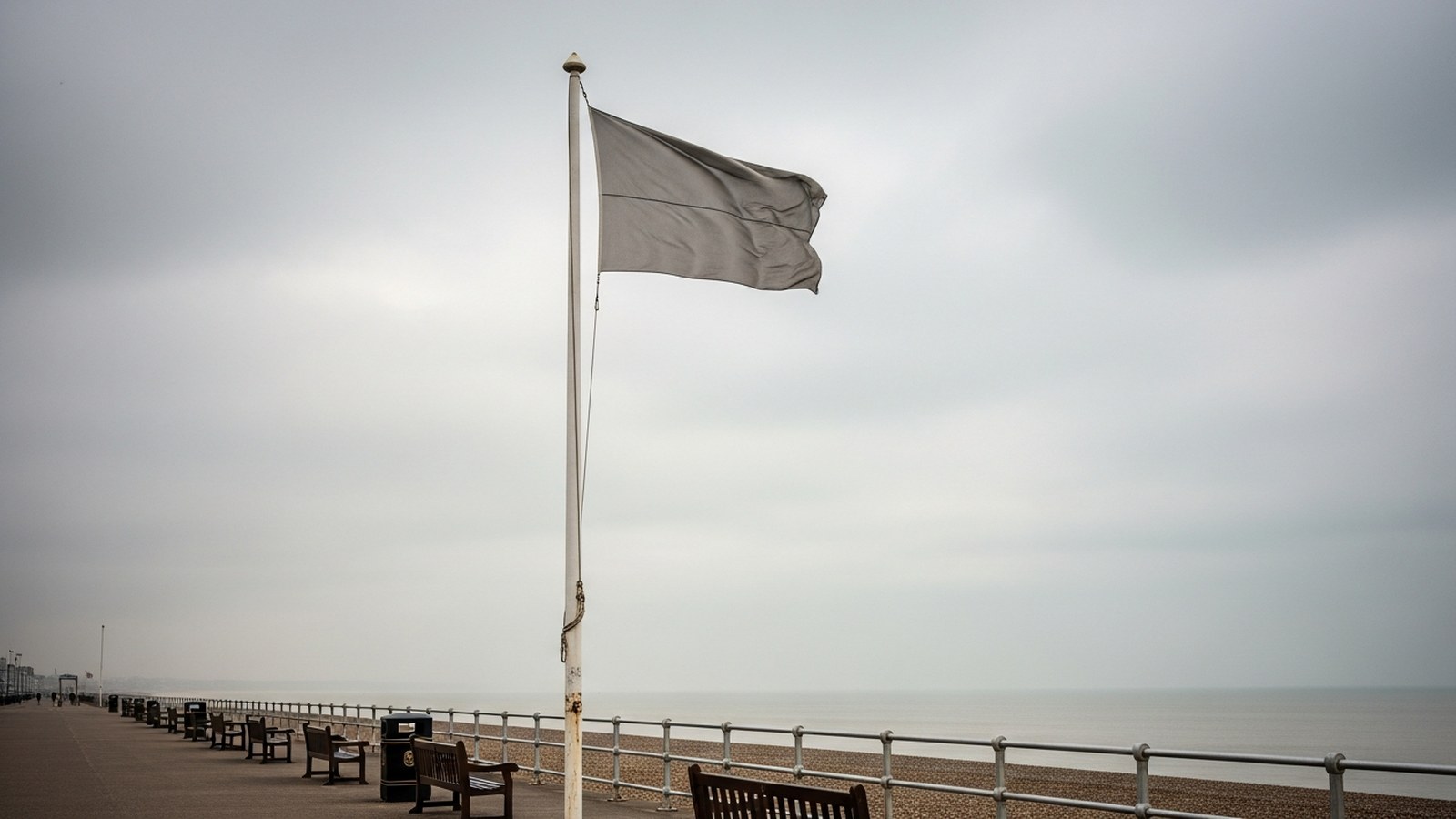 A faded flag hanging limp over an empty grey seafront