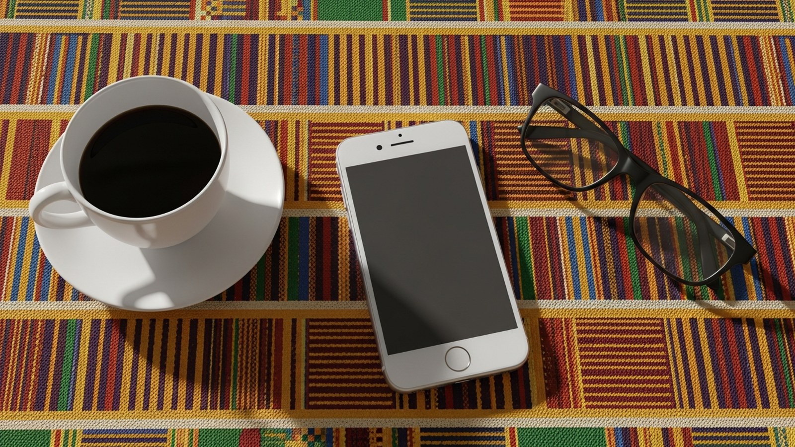Coffee, face-down phone and glasses on kente cloth